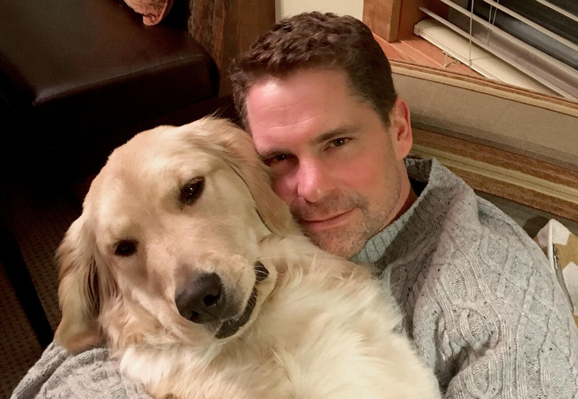 Mike McClay hugs his golden retriever while they both look at the camera.