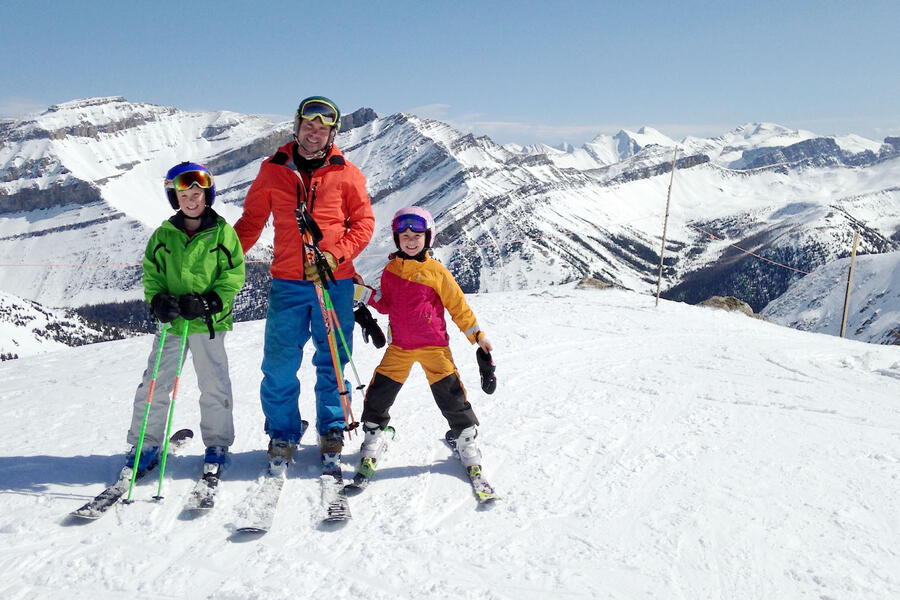 Mike McClay skiing with his two young kids on a mountain top, and all stopped to pose for a picture.